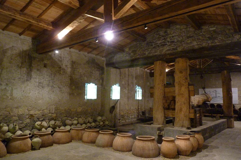 Grande salle avec les amphores de fermentation et, au fond, le pressoir romain reconstitué