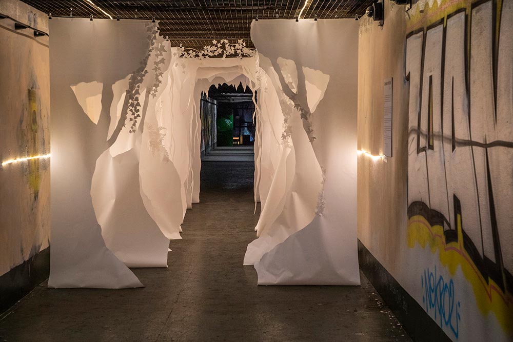 Les silhouettes d’arbres de papier blanc crées par Tine ouvrent la visite dans un long tunnel ponctué de graffitis
