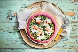 Pizza houmous au basilic, stracciatella di burrata, sauce vinaigrée à la framboise Le secret de sa pâte rose : des concentrés de betterave et de carotte. En garniture : un houmous au basilic, des spots de stracciatella di burrata, des feuilles d’épinard et des cranberries séchées. Le tout assaisonné par une sauce vinaigrée à la framboise.