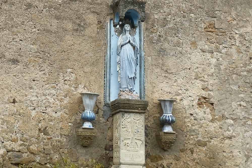 Une statue de la Vierge, au-dessus d’une reproduction du fameux pilier d’autel retourné par l’abbé, orne un mur aveugle de la villa Béthanie