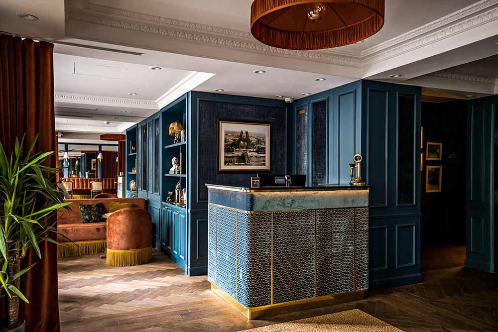 Lobby : Comptoir d’accueil sur-mesure « LBM » habillé de tissu « Misia » - Parquetà chevron - Suspension en velours plissée « Aurélie Cousin » - Peinture « Argile & Naé - Bibliothèque sur mesure.