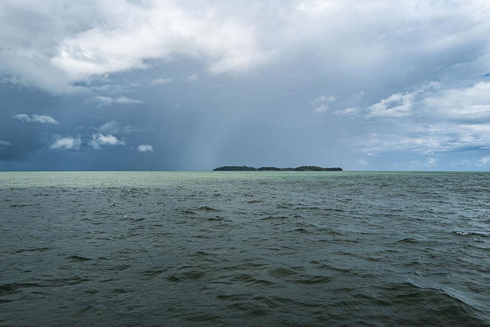 En approchant par la mer, les Îles du Salut surgissent peu à peu, silhouettes basses et mystérieuses sous un ciel chargé.
