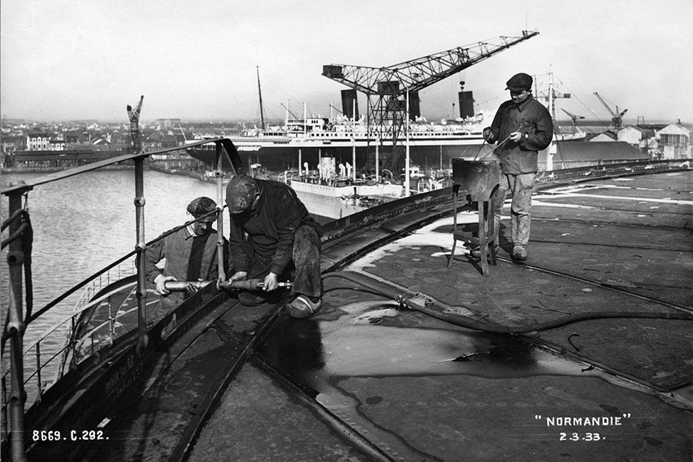 Des ouvriers en sabots travaillent sur le bastingage du pont des embarcations.