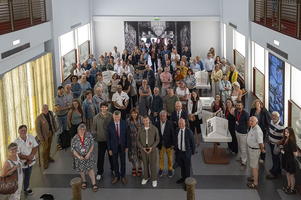 Photo souvenir pour les personnalités et les invités avec, au fond une immense photo de la salle à manger de première classe de Normandie. Au premier plan : Agathe Bodin, Lucas d’Aram, Éric Freysselinard, Cécile Schall, Adrien Motel, David Samzum, président de Saint-Nazaire Agglomération Tourisme, Pierre Sabouraud, directeur de Saint-Nazaire Agglomération Tourisme.
