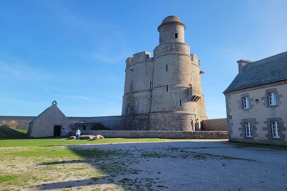 Tatihou - La tour Vauban vue depuis l’intérieur des fortifications. A sa droite, une chapelle qui a aussi servi de réserves. A sa gauche, d’anciennes casernes aujourd’hui transformées en musée. 
